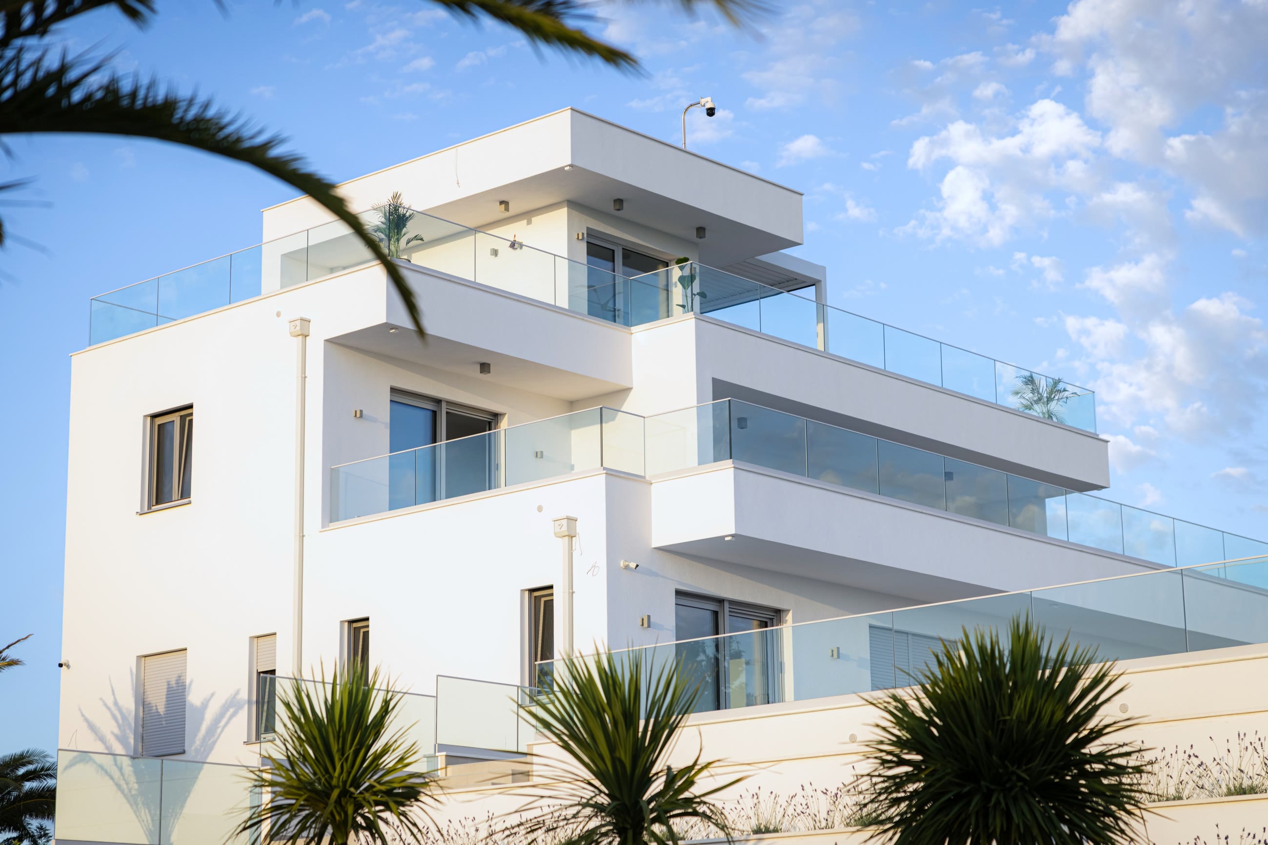 Villa ZenIt's white facade and glass balustrades seen through palm fronds